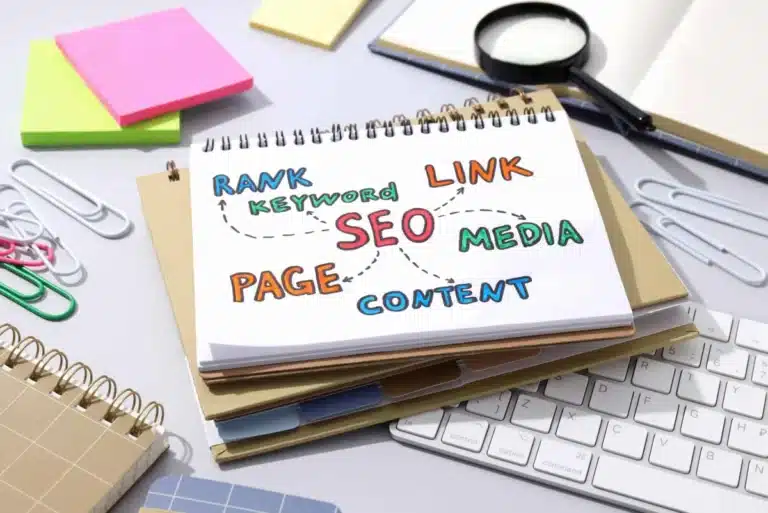 Τι είναι η θέση στη Google και πώς μετριέται το SERP rank - SEO - Οργανική Απήχηση Notebook page with colorful SEO terms (SEO, content, keyword, page, link, media) connected by arrows on a desk near a keyboard.