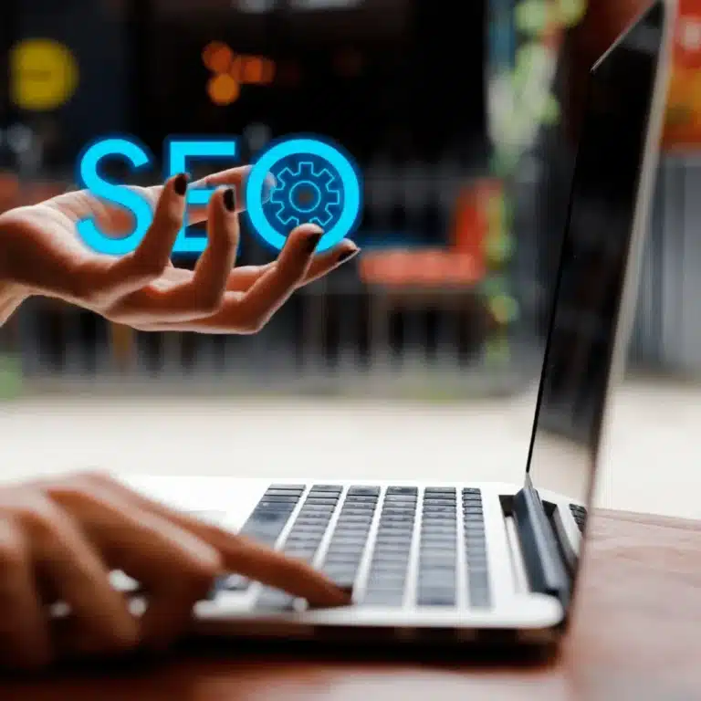 Person using a laptop with a glowing blue 'SEO' hologram and gear icon to represent search engine optimization.