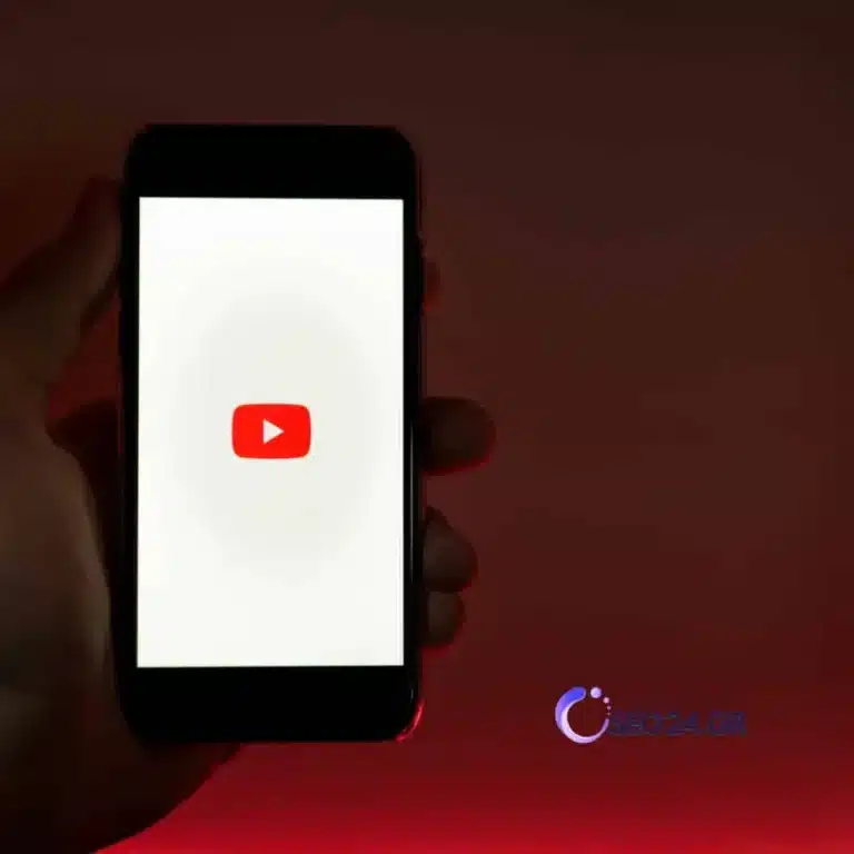 YouTube SEO τίτλοι περιεχόμενο και μετρήσεις που έχουν νόημα - SEO - Οργανική Απήχηση Hand holding a smartphone displaying the YouTube logo on a white screen against a dark red background.